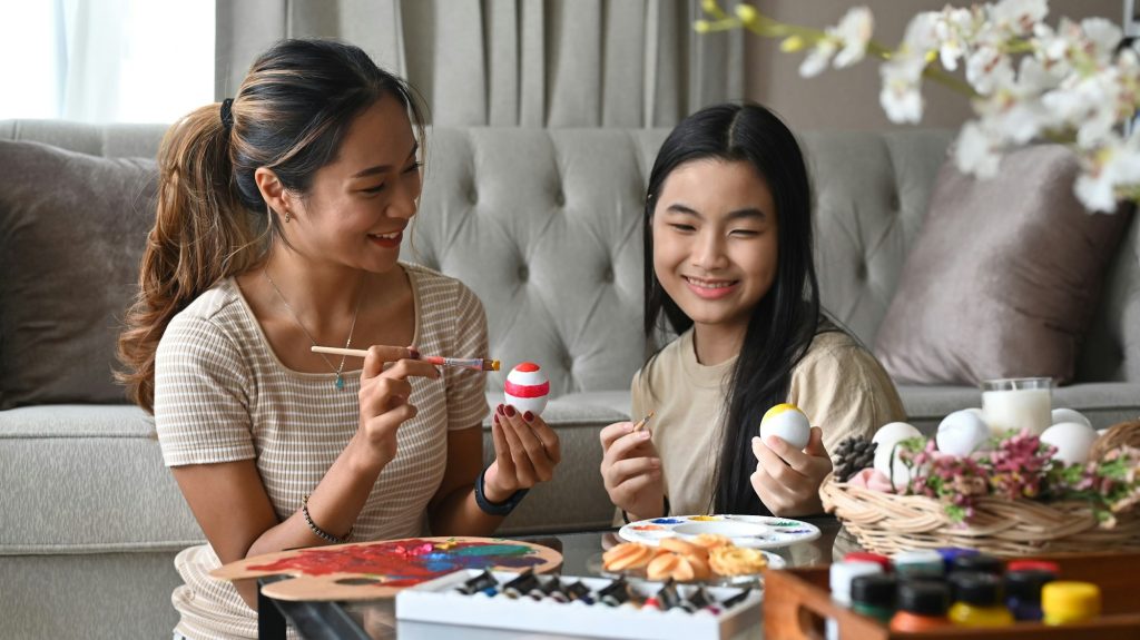 Asian young mother and daughter painting eggs preparing for Easter celebration.