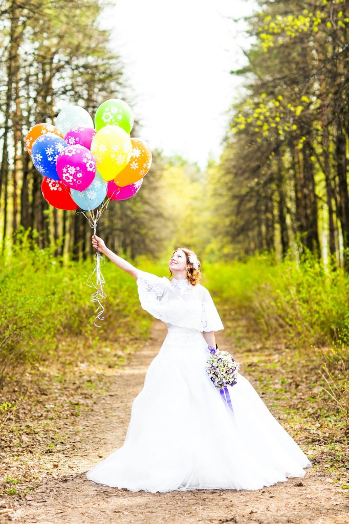 Cheerful bride with bunch of balloons outdoor
